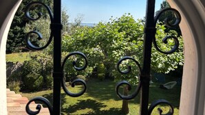 Visão através de um portão de ferro forjado com um jardim e céu claro.