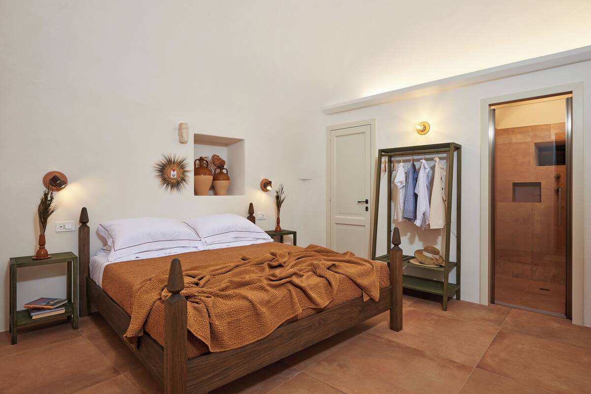 A bedroom with a wooden bed, bedside tables, a mirror, a wardrobe, and a door leading to a bathroom.