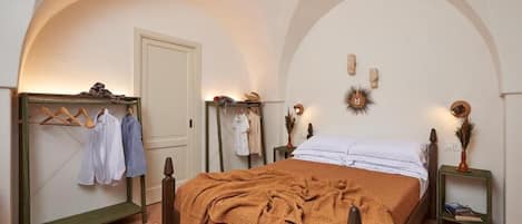A bedroom with a bed, a wooden wardrobe, a clothing rack, and a small bedside table with a lamp.