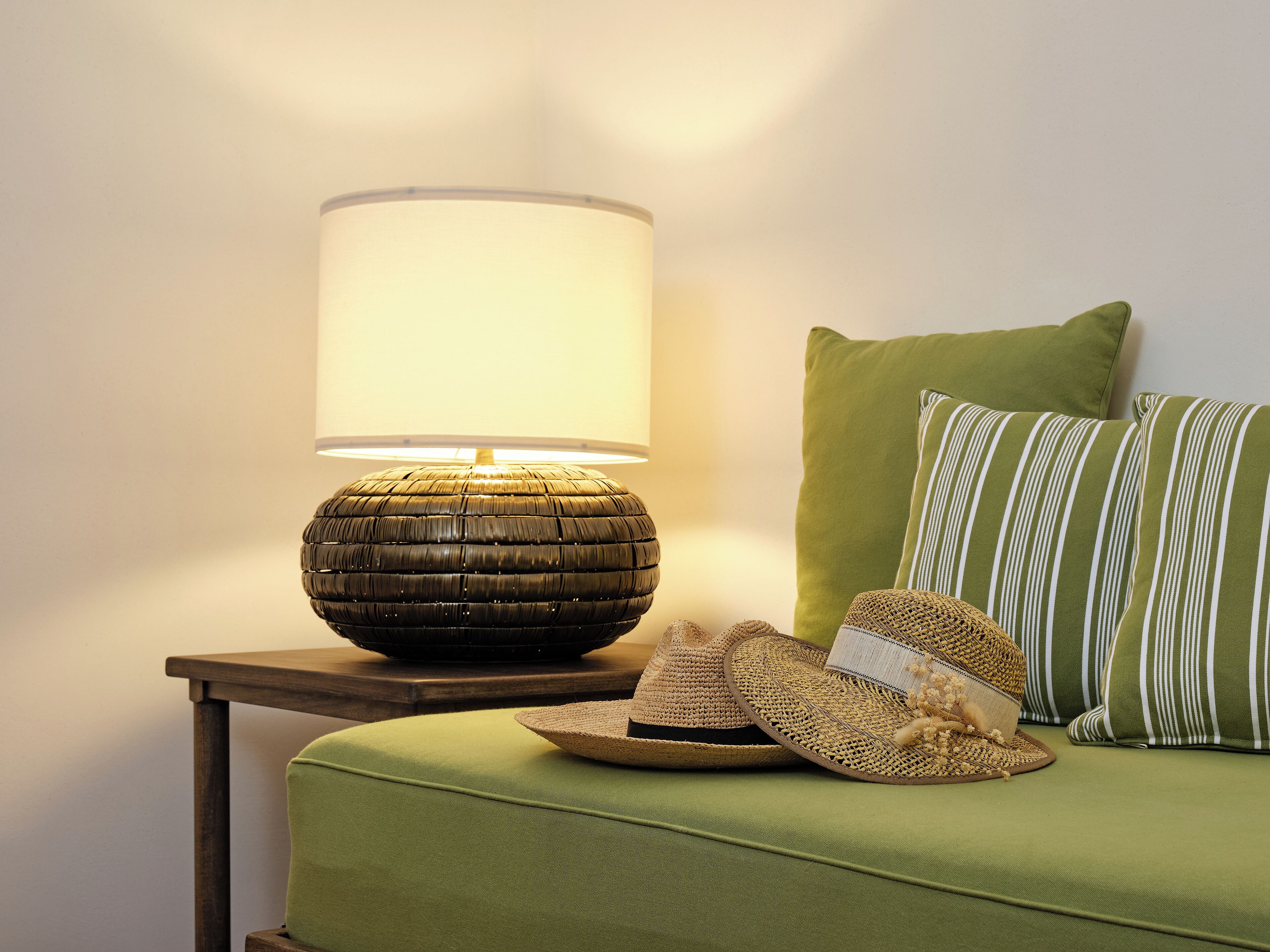 Een kamer met een groene bank, een lamp met een gevlochten voet, en een gestreept kussen.