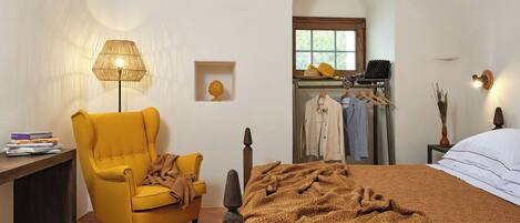 A bedroom with a bed, a chair, a lamp, a shelf with books, and a window.