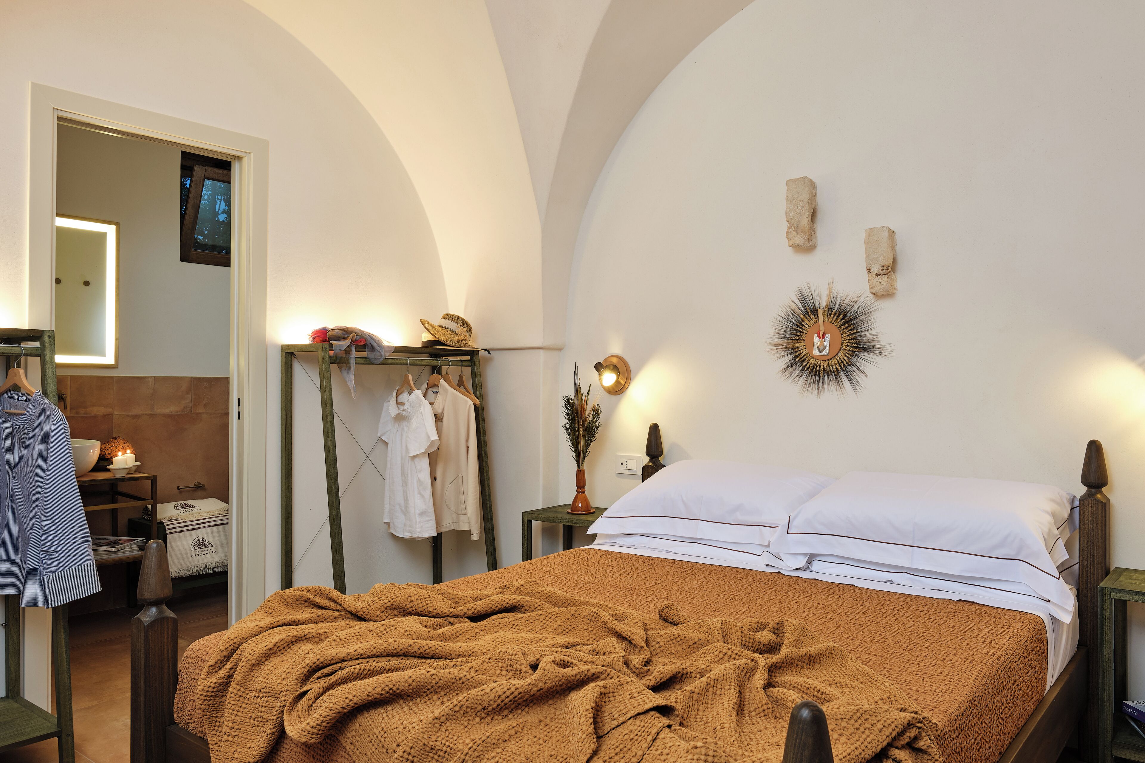 Een slaapkamer met een bed, nachtkastje, een wandlamp, spiegel en een garderobe.