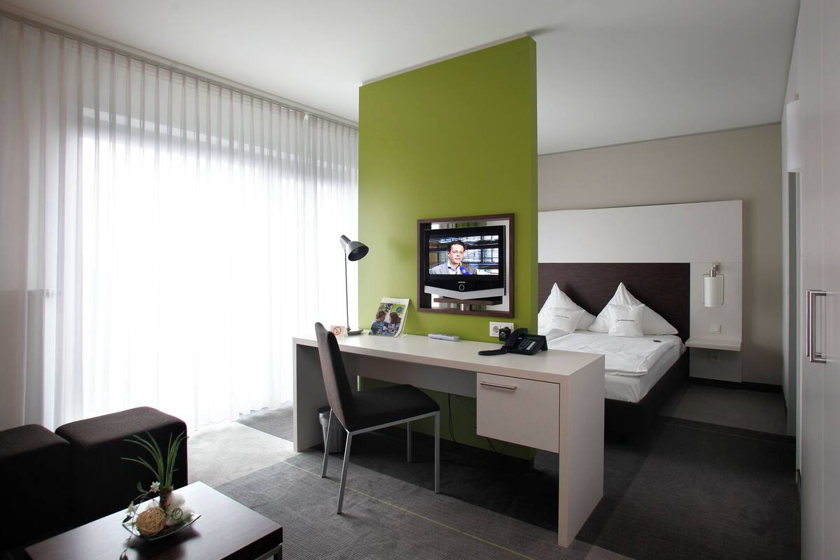 Una habitación de hotel con escritorio, cama, televisor y ventana con persianas.