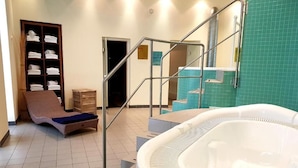Uma área de spa com hidromassagem, uma espreguiçadeira, uma prateleira de madeira com toalhas e uma escada para uma área de chuveiro.