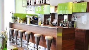 Uma área de bar com banquetas, balcão e prateleiras com garrafas e copos.