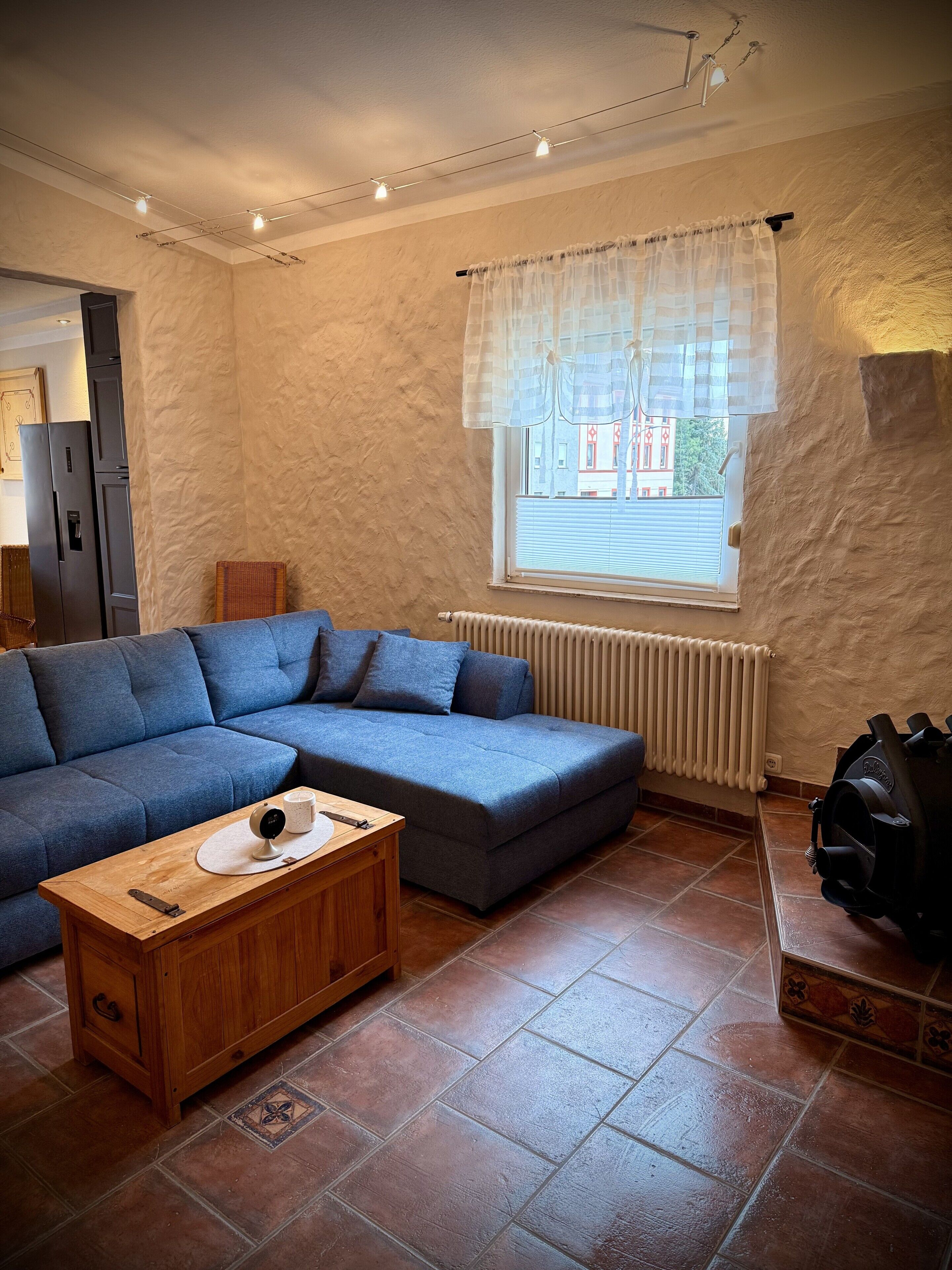 A living room with a blue sofa, a wooden coffee table, a radiator, and a window with curtains.