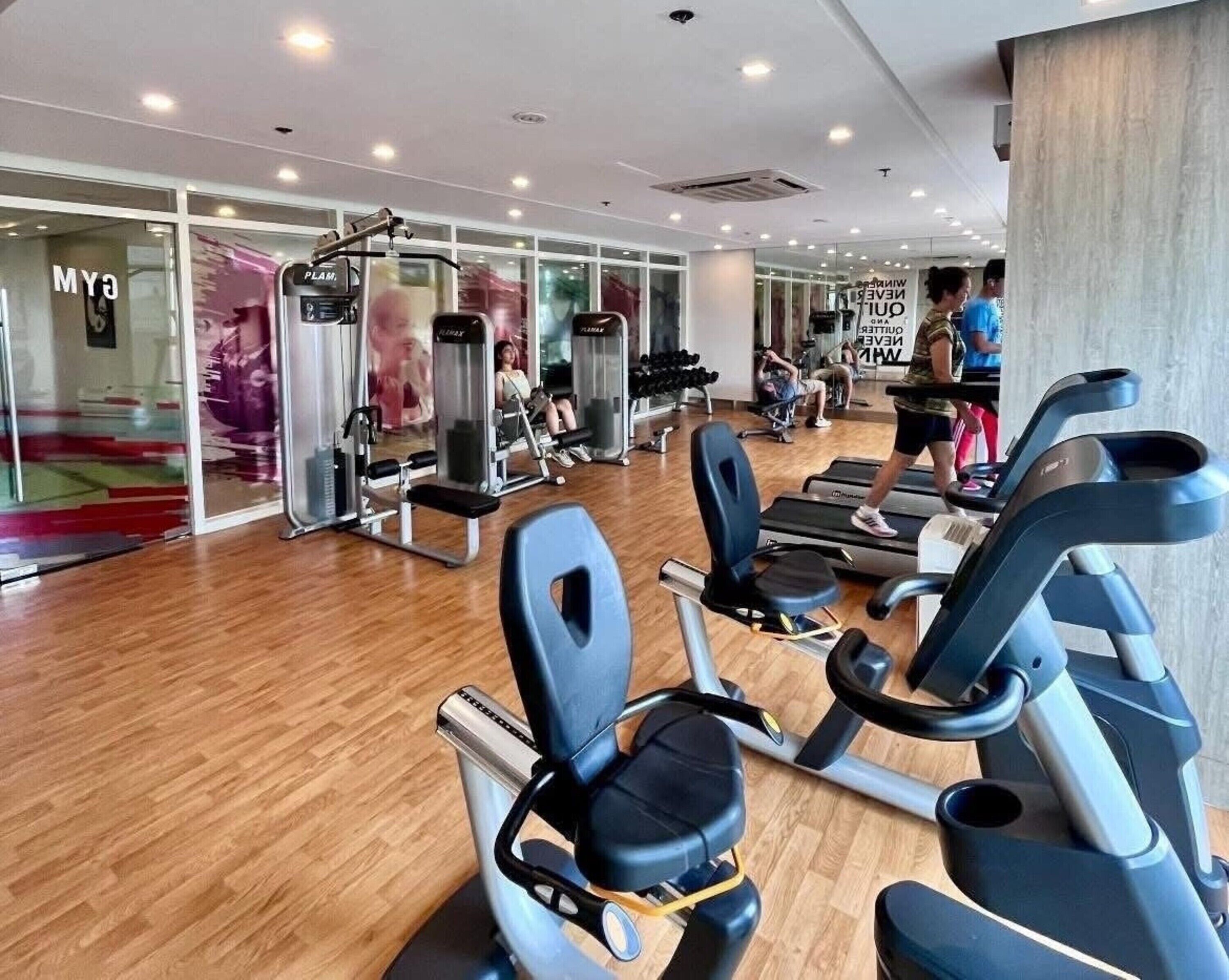 A gym with exercise equipment, a mirror wall, and a wooden floor.