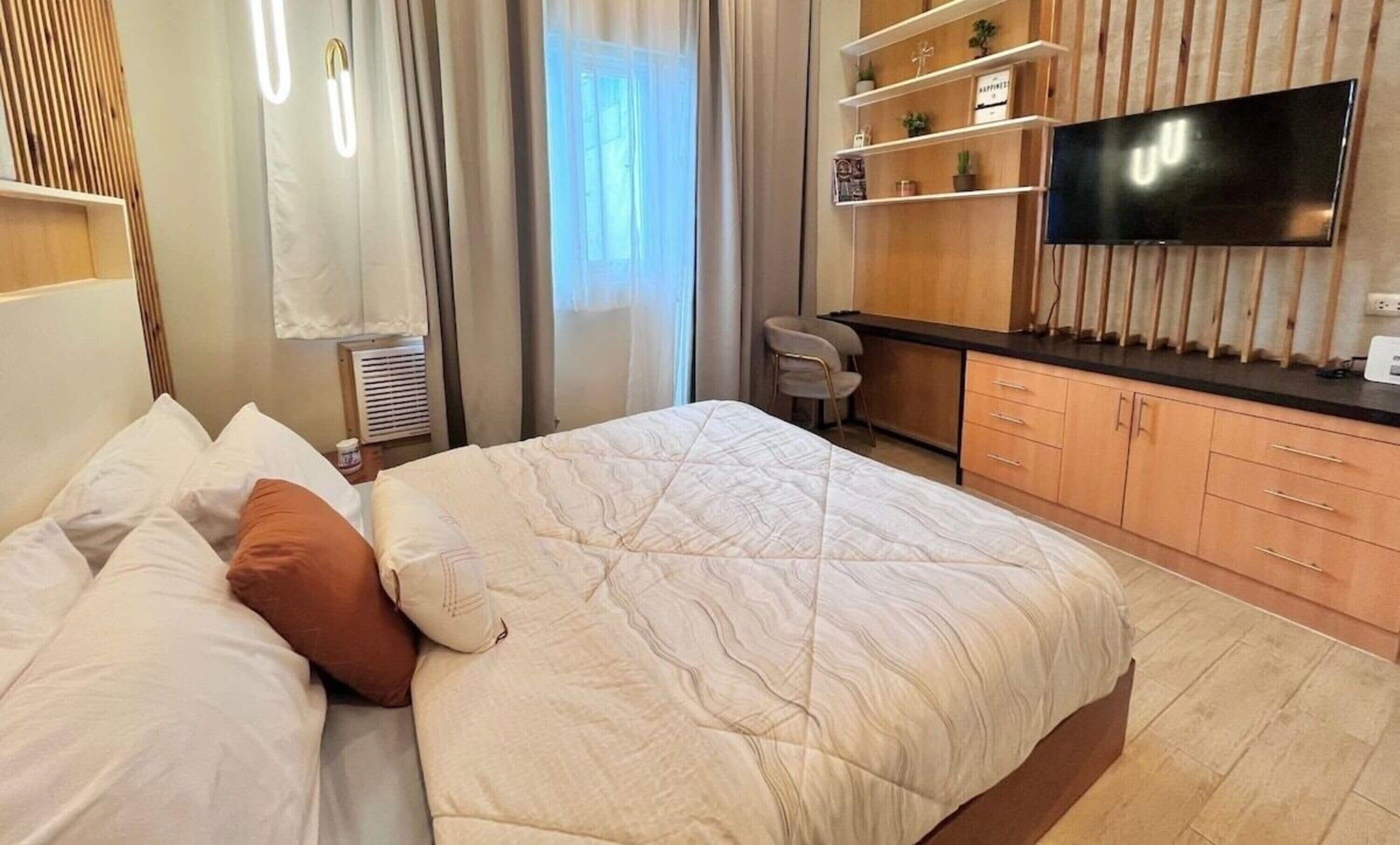 A modern hotel room with a large bed, a desk, a flat-screen TV, and built-in shelving.