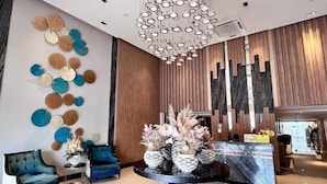 A modern lobby with a marble reception desk, blue upholstered chairs, a decorative wall, and a chandelier. - Cozy Studio at Lafayette Park (Iloilo)