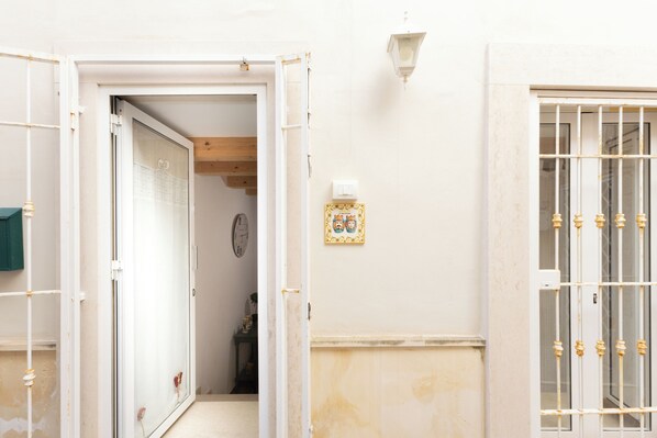Una porta oberta que dona a un passadís amb un rellotge i una taula petita amb una planta.