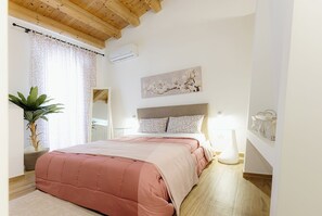Ein Schlafzimmer mit einem Bett, einer Zimmerpflanze, einem Gemälde und einem Nachttisch mit Lampe.