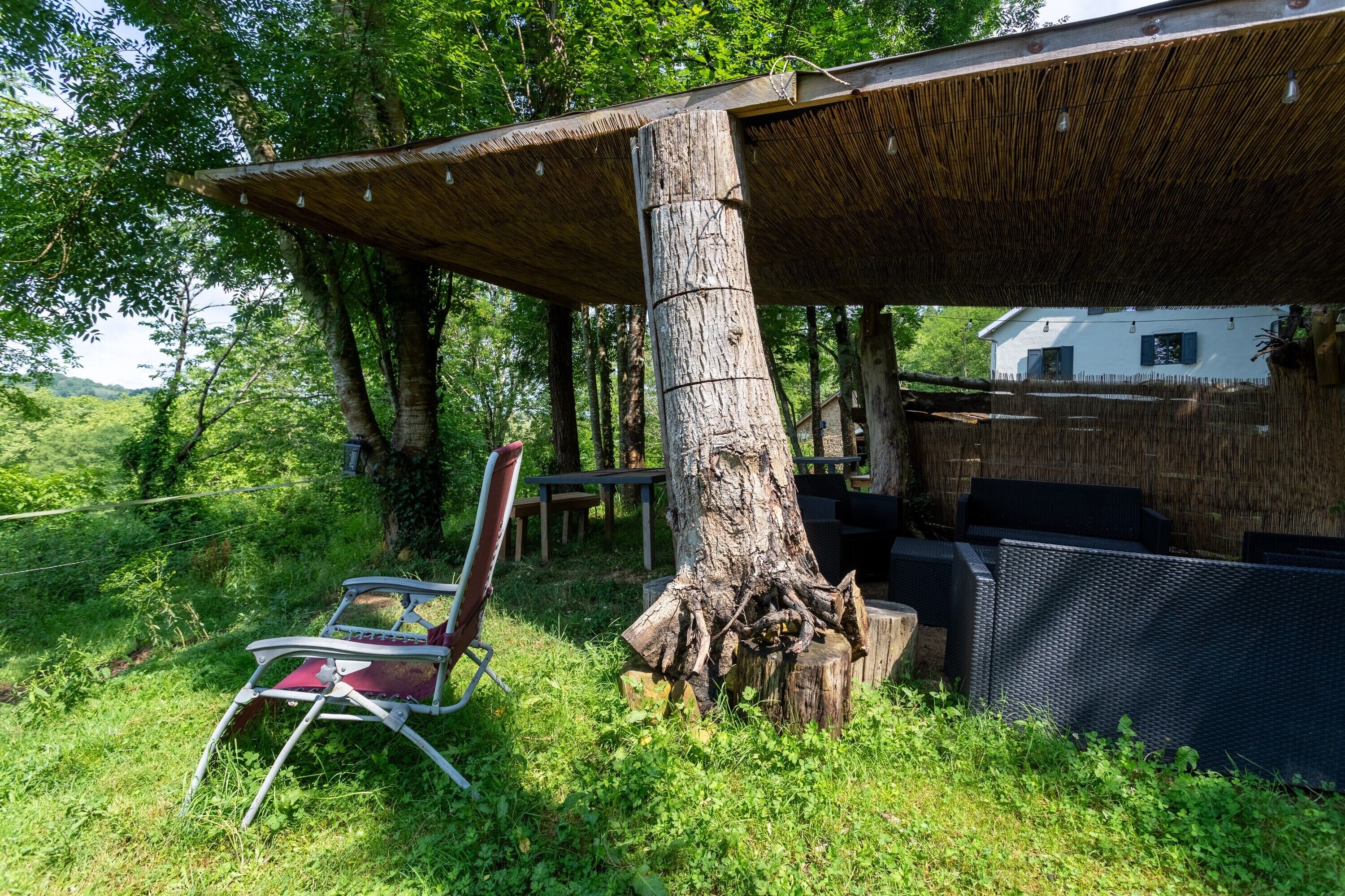 Un espacio de estar al aire libre rústico con techo de paja, una mesa de comedor y una silla.