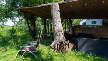 Un espacio de estar al aire libre rústico con techo de paja, una mesa de comedor y una silla.