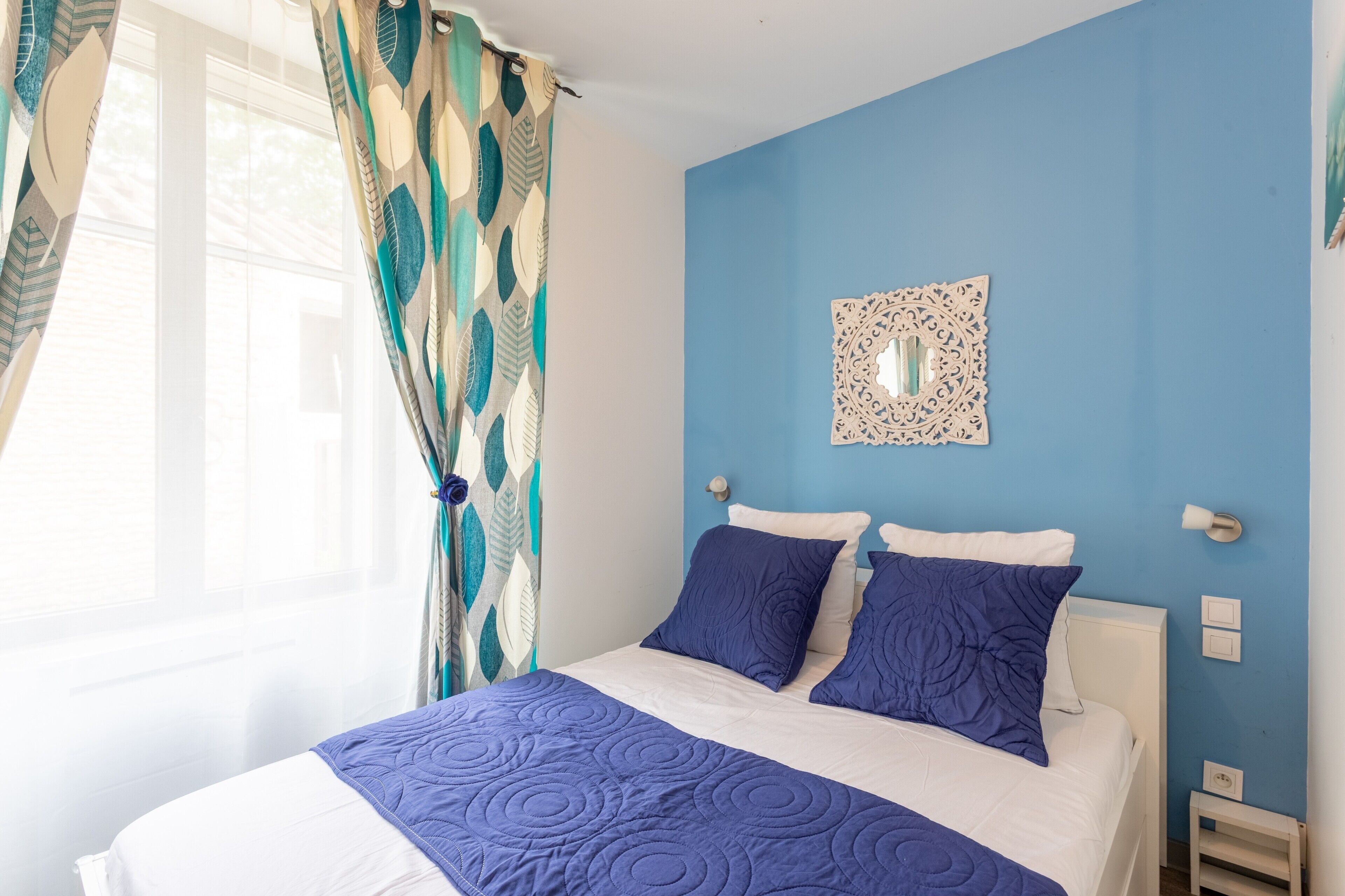 Una cama con un edredón azul, una almohada blanca y un adorno de pared.