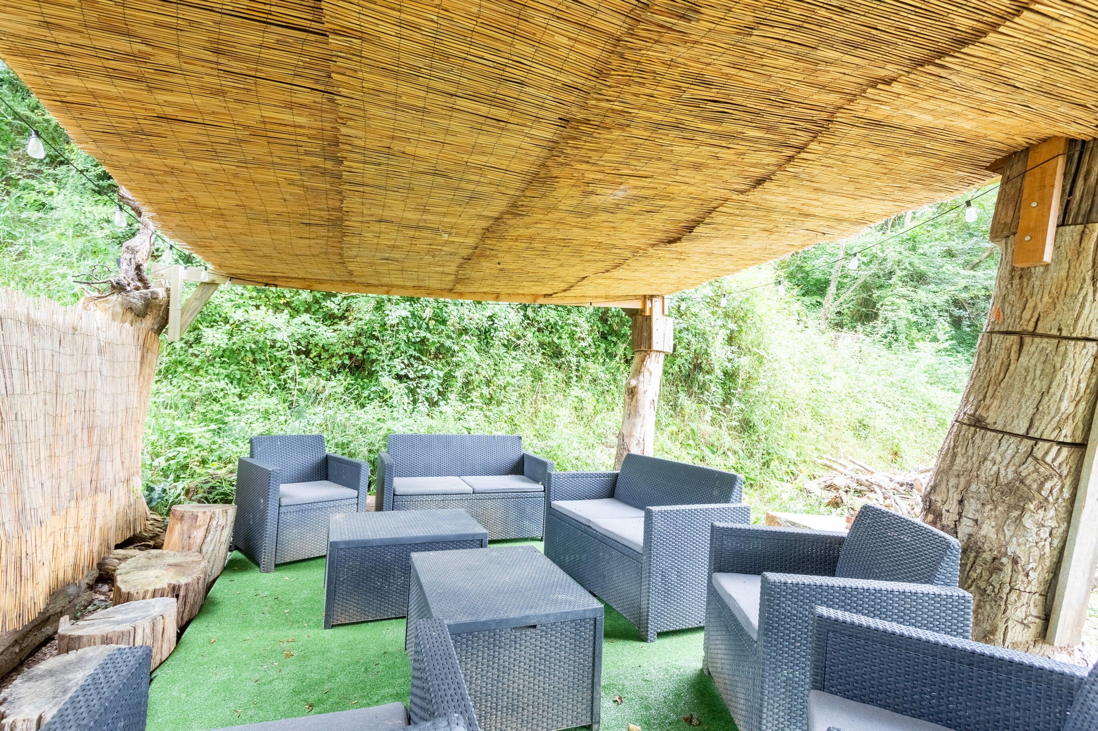 Eine Terrasse im Freien mit Korbmöbeln, einem Reetdach und künstlichem Rasen.