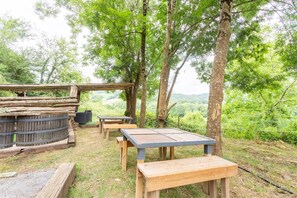 An outdoor seating area with wooden tables and benches, surrounded by trees and a view of the landscape. - Gîte "Donoma" at Domaine Helaku: Green Oasis with Countryside Views (Monein)
