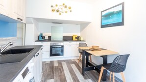 A modern kitchen with a sink, stove, and coffee maker, a dining area with a table and chairs, and a wall-mounted clock.