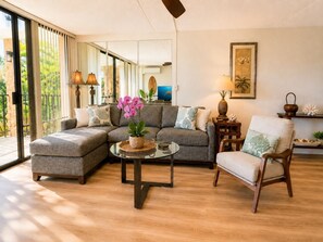 Ein modernes Wohnzimmer mit einem Ecksofa, einem runden Couchtisch, einem Holzstuhl und einer Glastür, die auf einen Balkon führt.