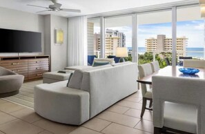 Ein modernes Hotelzimmer mit großem Fenster, Flachbildfernseher, einer Couch, einem Esstisch und einem Deckenventilator.