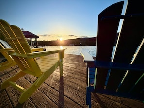 Eine Holzterrasse mit zwei gelben Adirondack-Stühlen, die auf ein Gewässer ausgerichtet sind.