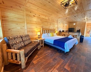 Ein Holzhütten-Innenraum mit Bett, Sofa und einer kleinen Küchenzeile.