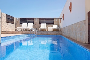 Una piscina con bordes de azulejos, sillas de descanso y un muro de piedra con detalles decorativos.