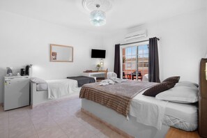Habitación de hotel con cama, escritorio, silla, televisor, equipo de aire acondicionado y vistas al exterior.