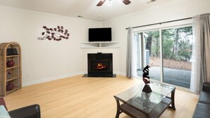 A living room with a fireplace, a television, a ceiling fan, and a large window. - Modern Charleston Getaway (North Charleston)