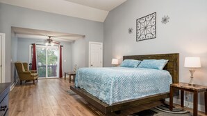 A bedroom with a bed, two bedside tables, a chair, a ceiling fan, and a view through a glass door to an outdoor area. - Modern Charleston Getaway (North Charleston)