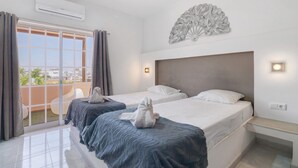 A hotel room with two beds, a balcony with a view, an air conditioning unit, and a decorative wall piece. - Room 'South Side Guesthouse - Quarto E' with Shared Pool, Wi-Fi and Air Conditioning (Quelfes)