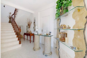 Una escalera con balaustres de madera, una puerta blanca, un estante de vidrio con adornos y una pared con textura.