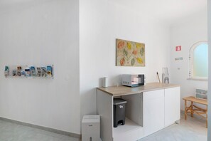 Una habitación limpia y moderna con kitchenette, un cubo de basura, un microondas y una pequeña mesa.
