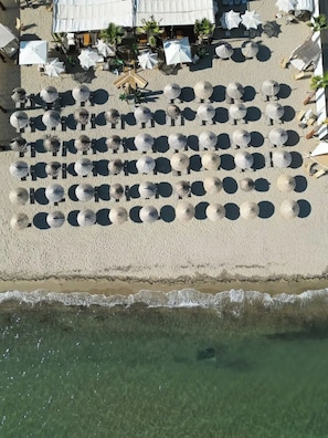 Vista aérea de una playa con hileras de sombrillas y sillas reclinables, arena y una vista despejada del océano.