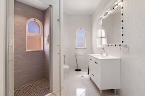 Casa de banho moderna com cabine de duche em vidro, lavatório branco com espelho e sanita.