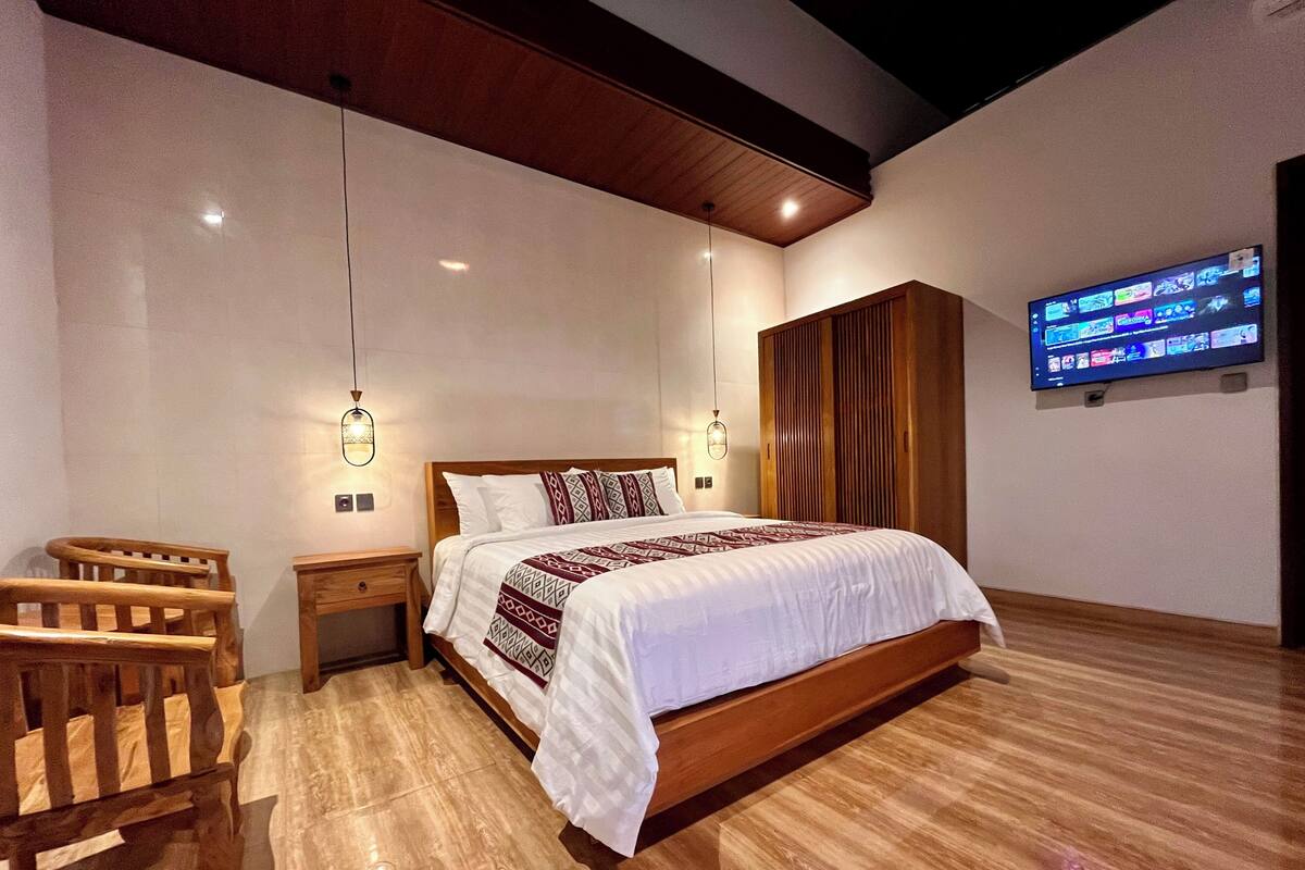A bedroom with a wooden bed, bedside tables, a TV mounted on the wall, and a wooden chair.