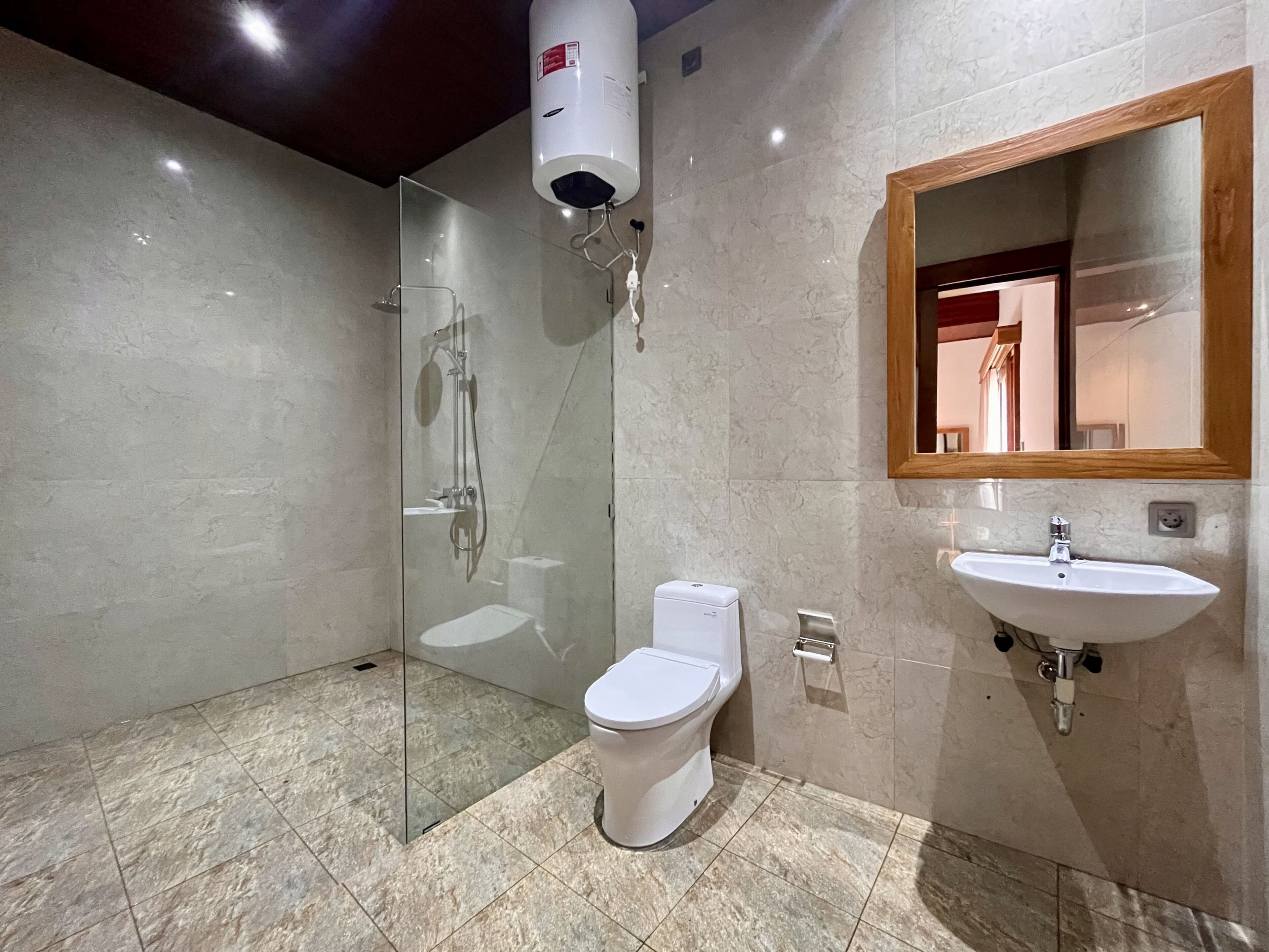 Ein modernes Badezimmer mit einer gläsernen Duschkabine, Toilette und Waschbecken mit einem spiegel mit Holzrahmen.
