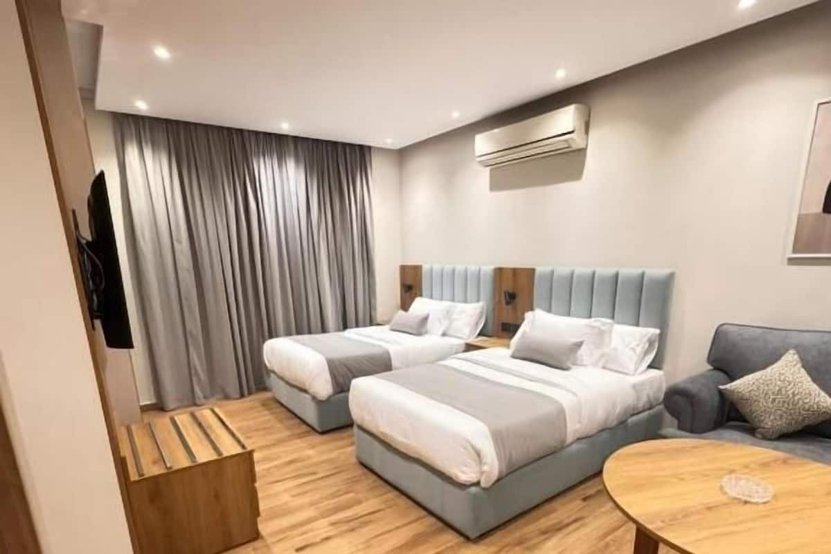 A modern hotel room with two beds, a sofa, a round table, and a TV.
