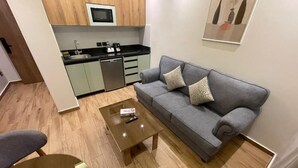 Un espacio habitable compacto con kitchenette, sofá gris y una mesa de centro.