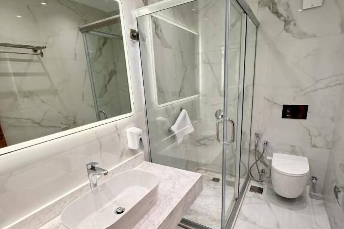A modern bathroom with a glass-enclosed shower, a large mirror, and a marble countertop.