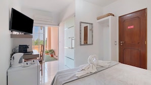 A hotel room with a bed, a television, a desk with a coffee maker, and a view of the outdoors. - Room 'South Side Guesthouse - Quarto W' with Shared Pool, Wi-Fi and Air Conditioning (Quelfes)