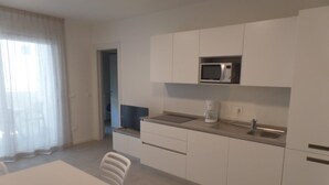 A modern kitchen with white cabinets, a microwave, a coffee maker, and a dining area with a table and chairs. - Modern Two-bed Flat With Shared Pool and hot tub (San Michele al Tagliamento)