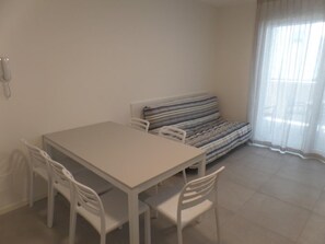 A room with a white table and four chairs, a striped sofa, a telephone on the wall, and a window with sheer curtains. - Modern Two-bed Flat With Shared Pool and hot tub (San Michele al Tagliamento)