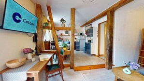 Ein Zimmer mit einem Holzesstisch, Stühlen, einem an der Wand befestigten Fernseher und einer Küche im Hintergrund.