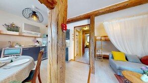 Ein gemütlicher Wohnbereich mit einer Couch, einem Esstisch und einer Küche mit Mikrowelle sowie Holzbalken.