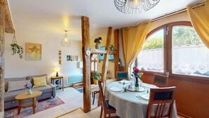 Ein gemütliches Wohnzimmer mit einer Couch, einem Esstisch für zwei Personen und einem Fenster mit Vorhängen.