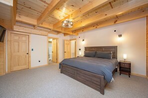 Ein Schlafzimmer mit Holzbalkendecke, einem Bett mit dunkelblauer Bettdecke, einem Nachttisch mit Lampe und einer Tür.