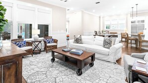 A spacious living room with a white sofa, a coffee table, and a dining area with chairs and a table. - NEW Designer WaterColor Home with Private Pool, Deluxe Outdoor Spaces, and LSV (Santa Rosa Beach)