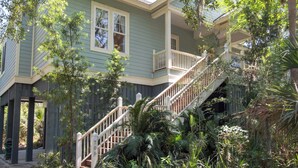 Una casa de dos pisos con una escalera que lleva a un balcón, rodeada de exuberante vegetación.