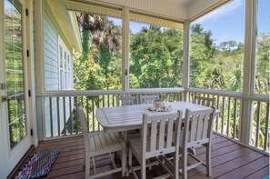 Eine überdachte Veranda mit Tisch und Stühlen, einem gemusterten Teppich und Blick auf üppiges Grün.