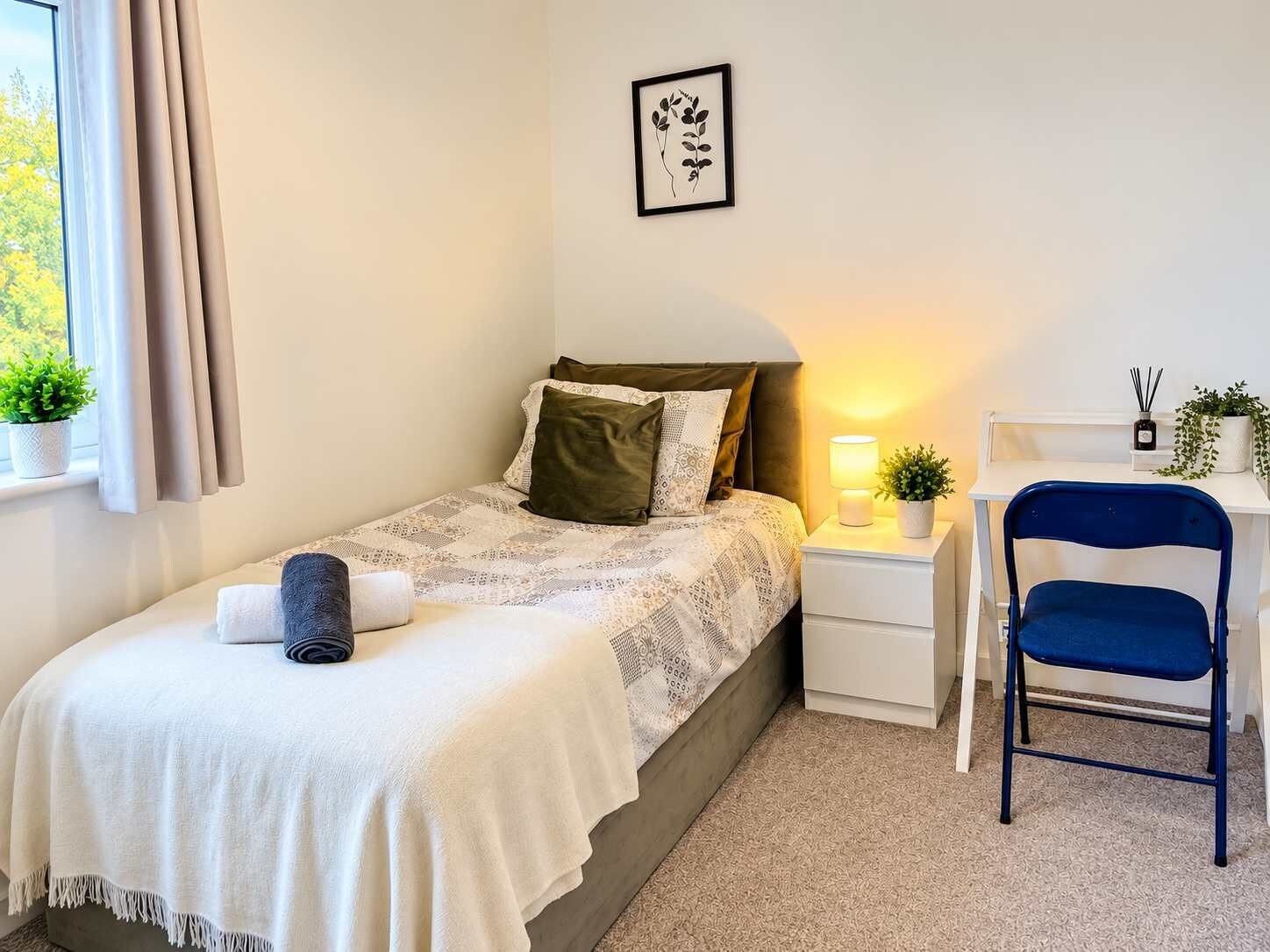 A neatly arranged bedroom with a bed, bedside table, chair, and a window with curtains.